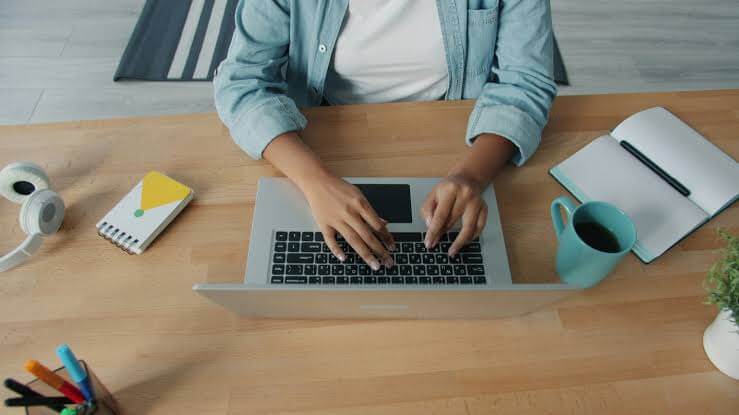 A person typing on a laptop at a wooden desk